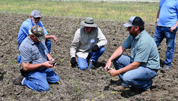 4 men kneeling in a recently plowed field with one man standing behind them