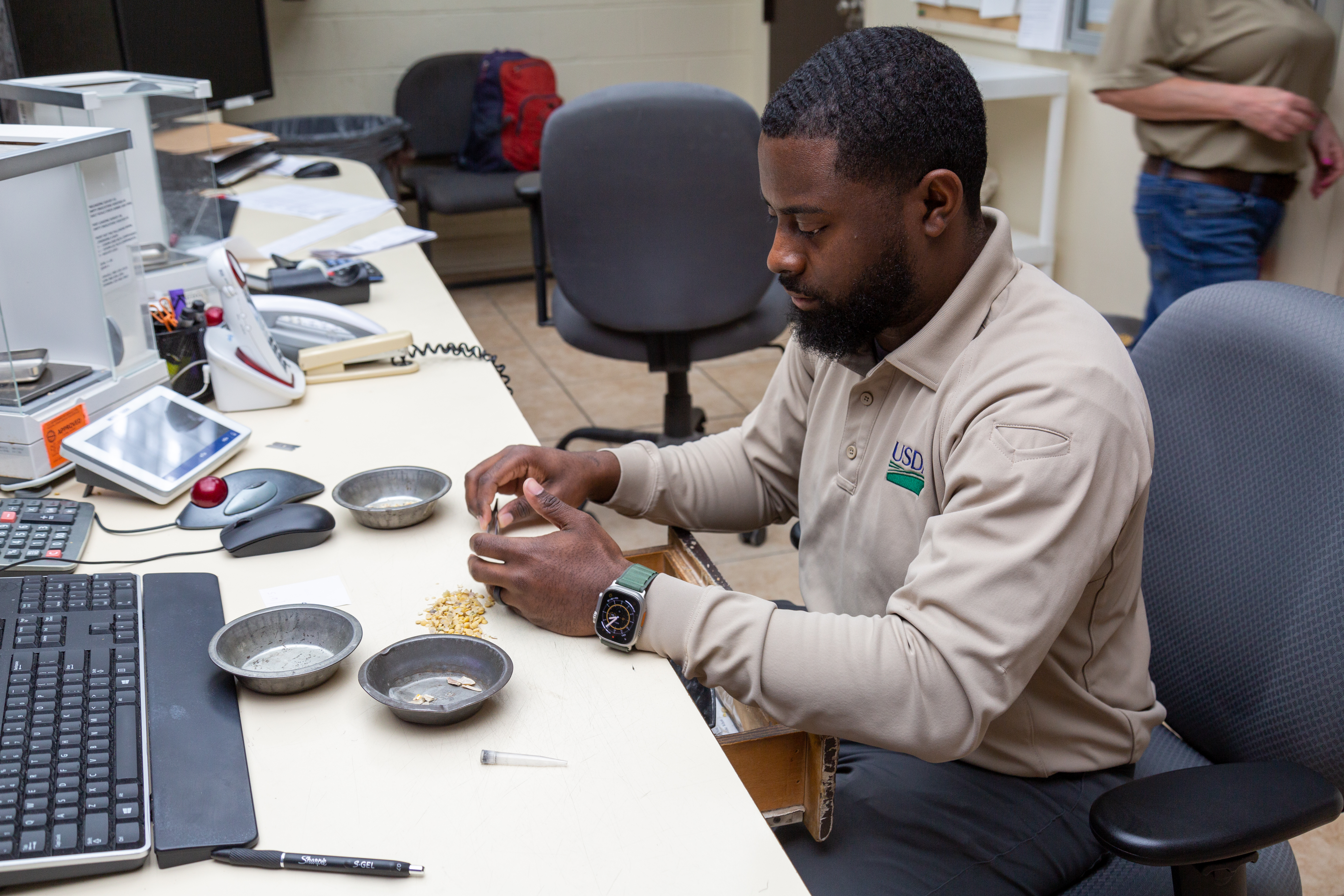 USDA employee sitting at a desk in front of a computer with a small pile of seeds