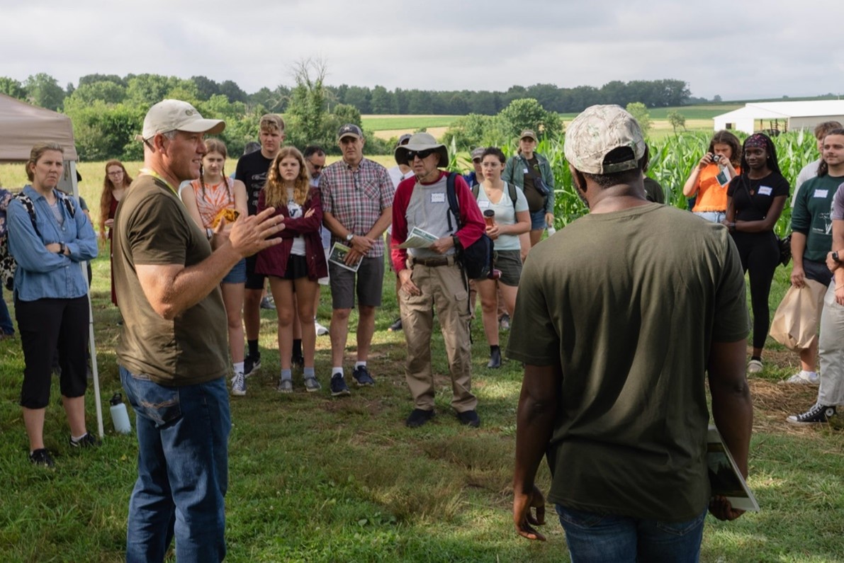 People standing in a field listening to a man talk.